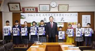 「令和2年度大崎市民憲章書道コンクール表彰式」と書かれてた横断幕の前で受賞者の小中学生が、書道の作品を持って、大崎市長と並んで写っている写真