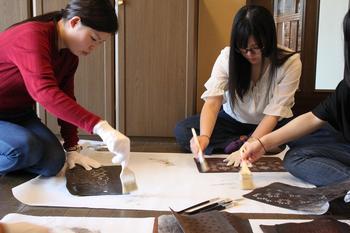 床に広げた模造紙に刷毛を使って小紋の柄を写している2人の女子大生の写真