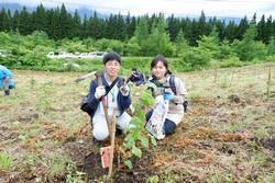 スコップを持った男性と青い軍手をしている女性が植樹をした苗木のそばにしゃがんで座っている写真