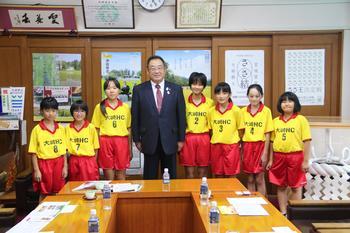 黄色の上着に赤い半ズボンのユニフォームを着た大崎ハンドボールクラブスポーツ少年団の皆さんが市長と並んで立っている写真