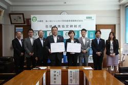 大崎市長と包括連協定を結ぶ企業の代表者の女性が協定書をもって立っており、その両脇に関係者が3名ずつ並んでいる写真