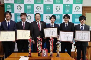 テーブルに置かれた縦と4つのトロフィー、伊藤市長と賞状を持って立っている5人の大崎4Hクラブのメンバーの写真