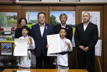 空手道着を着て、金メダルと賞状を手にしている笹原さん（右）と柴田さん（左）の後ろに大崎市長と関係者の方々が並んでいる写真