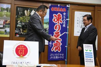 「凍り豆腐」ののぼり旗の前で登録証を授与する大崎市長（左）と、受け取る鈴木組合長（右）
