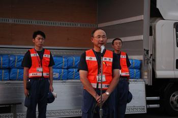 派遣職員を代表してあいさつするオレンジ色のベストを着た三浦防災安全課長とその後ろに2名の派遣職員が写っている写真