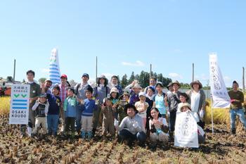 稲刈り後の田んぼで、参加者が集まって笑顔で写っている集合写真