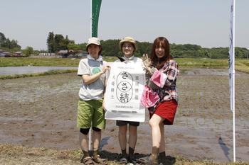 参加した奥口アナ、石垣アナ、名護アナが「ささ結」と書かれた白い布のようなものを持ち、のぼり旗の前で笑顔で立っている写真