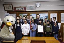受賞報告に訪れた鹿島台小学校ブラスバンドの皆さんがトロフィーと賞状を持って、市長と白い鳥のマスコットキャラクターと並んで写っている集合写真