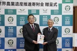 古川信用組合島谷理事長（右）と伊藤大崎市長が寄付金を持って並んで写っている写真
