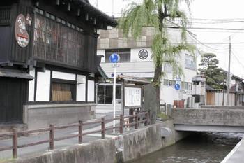 町に流れる川と柳の木、道路沿いに建っている昔ながらの日本家屋のつくりの建物の写真