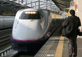 駅のホームに入ってきた新幹線と荷物をもって立っている乗客の写真