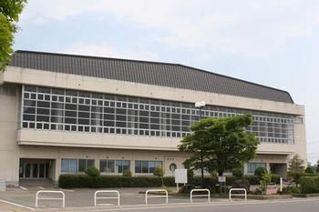 2階に柵のある窓があり、体育館の周りには緑の木々が植えられている古川総合体育館の外観写真