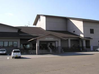 駐車場に車が2台停めてある、茶色の外壁をした岩出山文化会館の外観写真