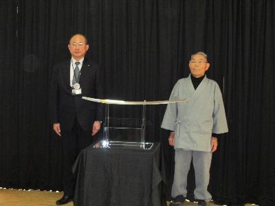 中央に新作太刀があり左側に松山総合支所長、右側に九代目法華三郎信房氏