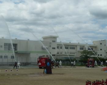 消防団員の方々が2階建ての建物に向かって2人1組で放水をしている防災訓練の様子の写真